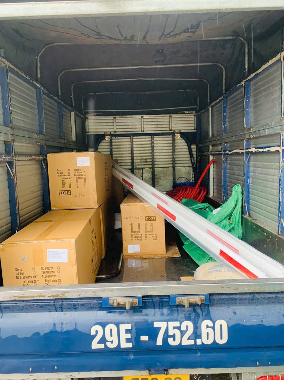 Thùng xe tải chở các thùng carton và thanh chắn barrier trắng đỏ cùng dụng cụ thi công
